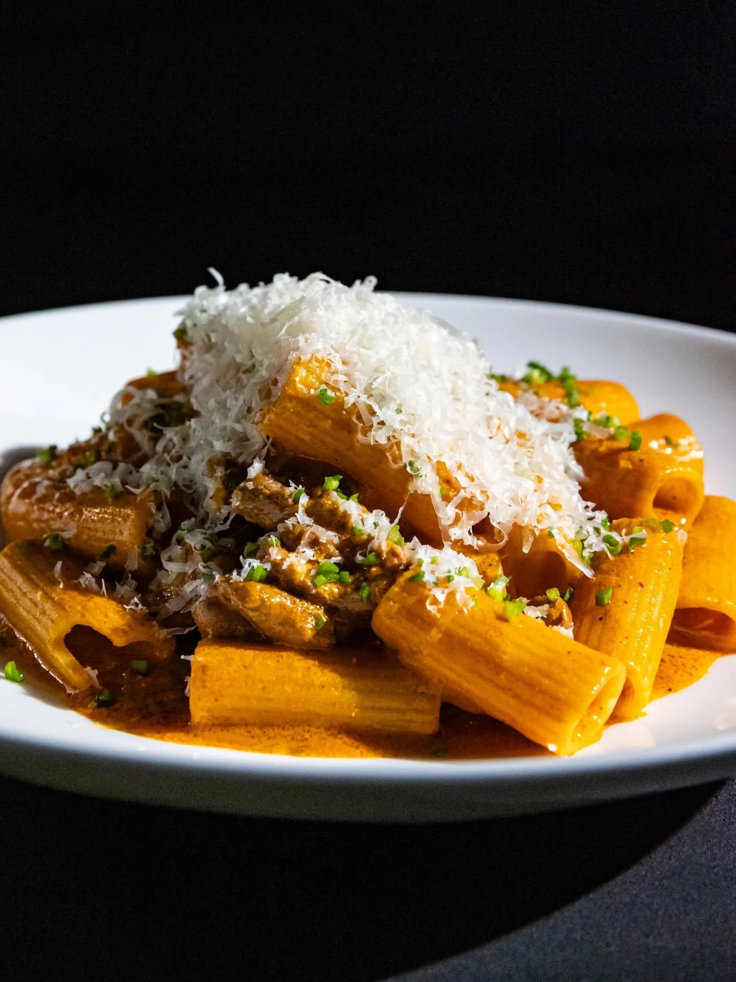 Plate of pasta with sauce, topped with shredded cheese and garnished with chopped herbs.