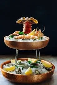 A two-tiered dessert display with assorted sweets, topped with strawberries, cookies, and garnished with lemon slices and mint leaves.