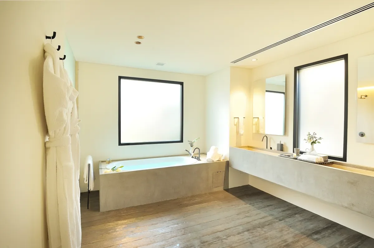 Modern bathroom with a large bathtub, a double sink vanity with mirrors, and frosted windows, decorated with towel racks and minimal decor.