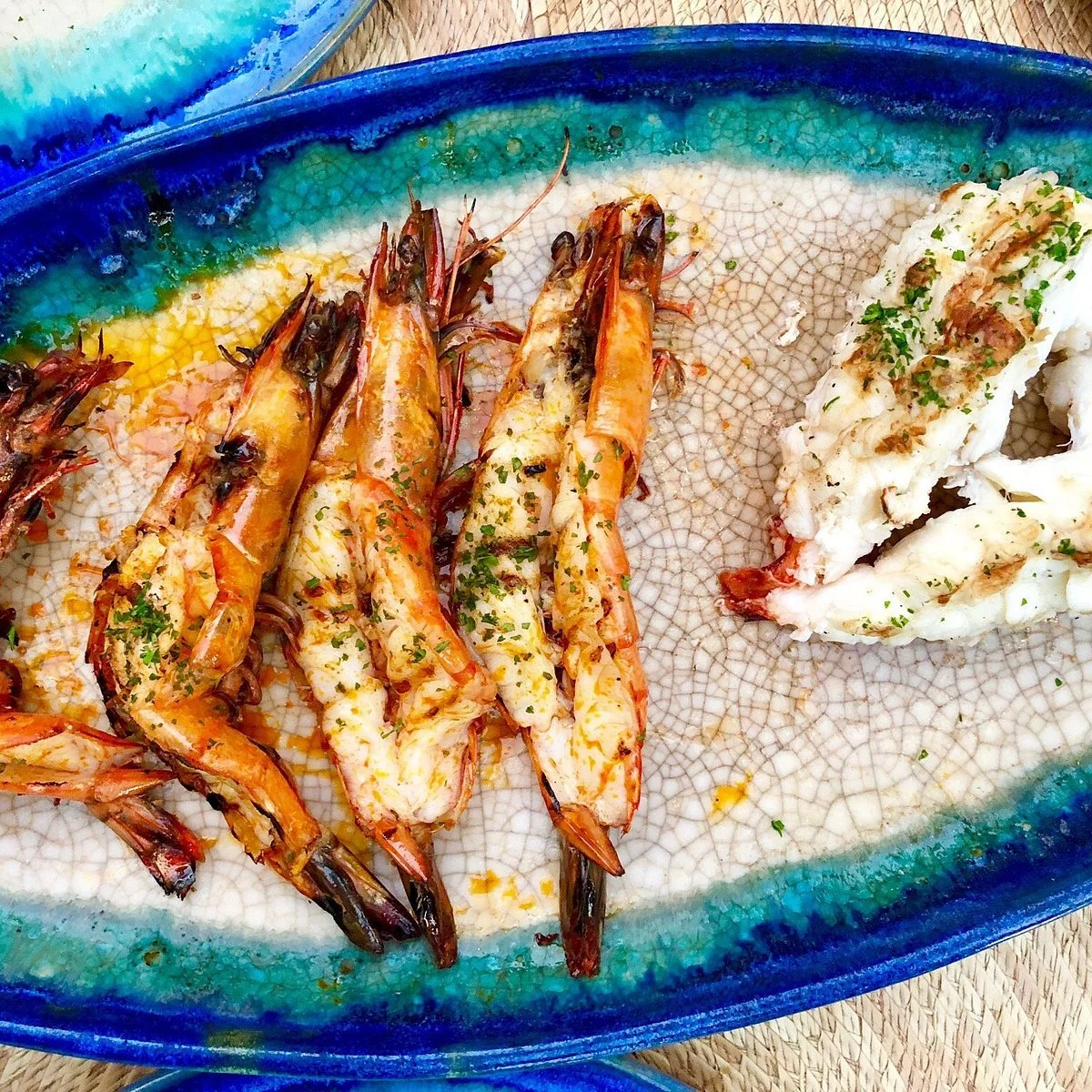 Roasted shrimp garnished with herbs on a decorative plate with a side of fish