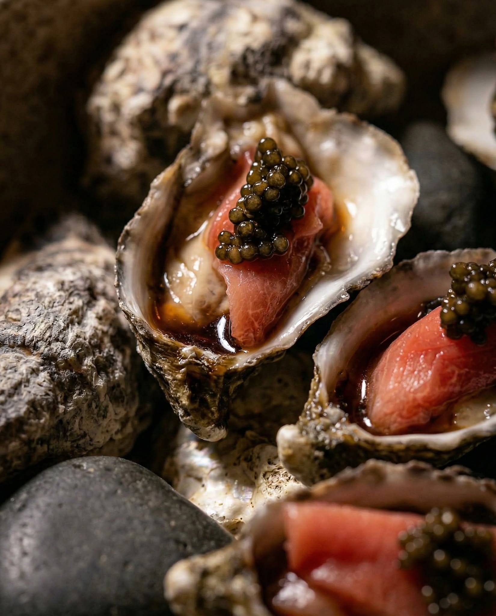 A close-up of oysters with some black caviar and slices of fish, possibly salmon, inside opened oyster shells.