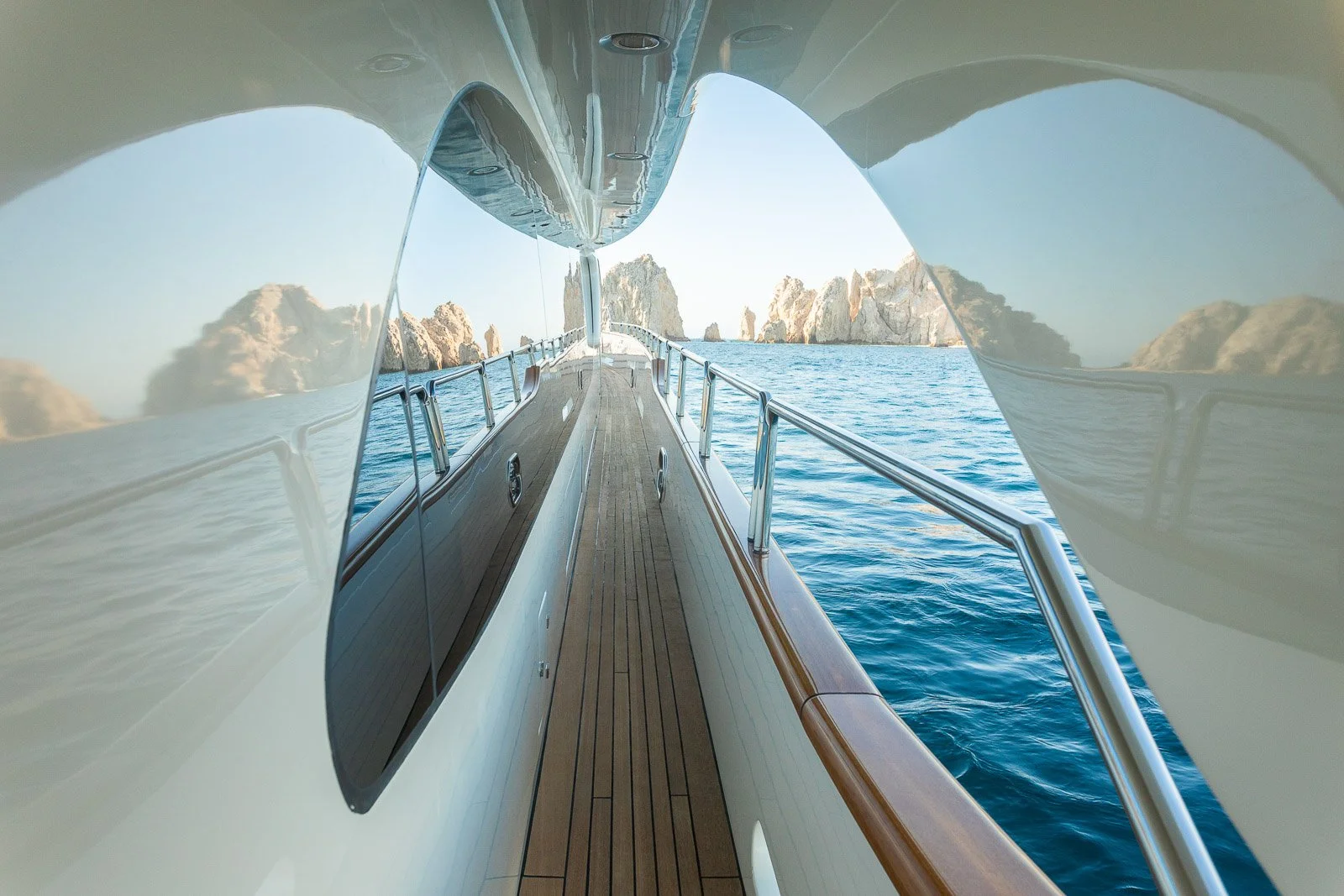 View from a yacht showing the deck and side windows with a rocky shoreline in the distance.