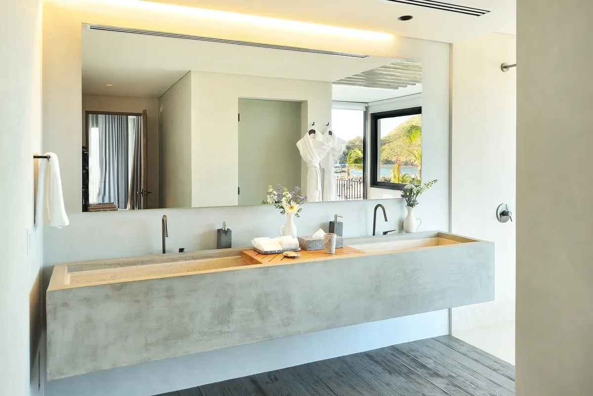 Modern bathroom with dual sinks, large mirror, and a window overlooking a scenic outdoor view with hills and water.