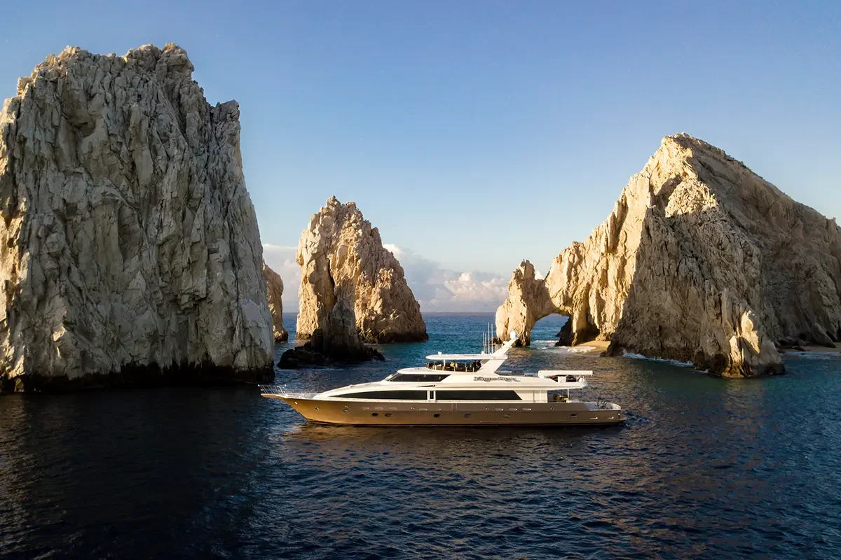A luxury yacht sailing near large rock formations in the ocean.