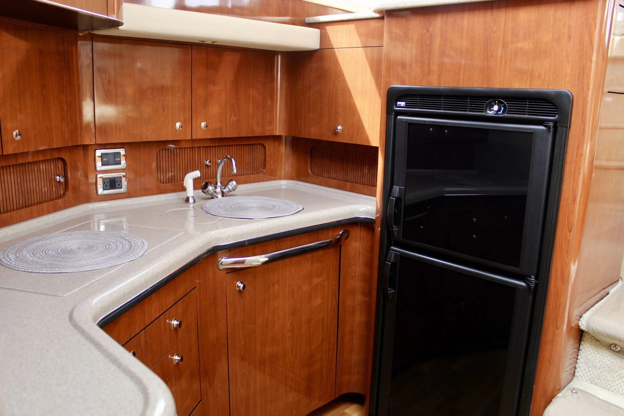 A kitchen with wooden cabinets and drawers, a beige countertop with circular placemats, a faucet, and a black oven or microwave built into the cabinetry.