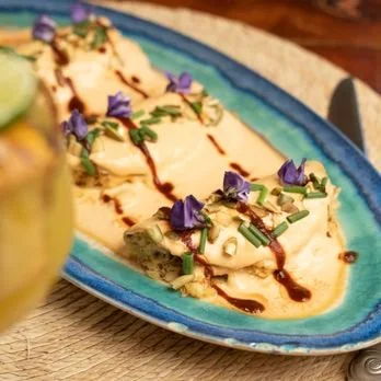 Dessert on a turquoise plate topped with edible flowers, chocolate drizzle, and chopped nuts.