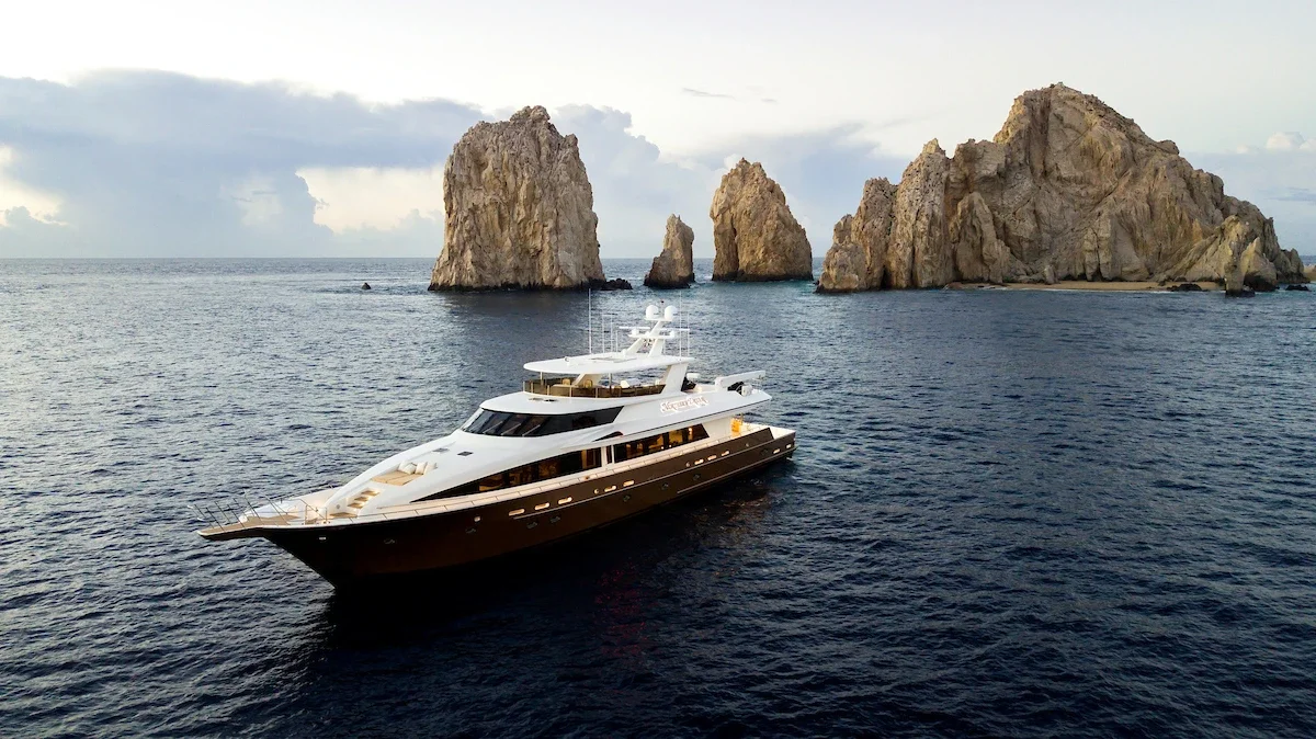 Luxury yacht sailing near rocky islands in the ocean under cloudy sky.