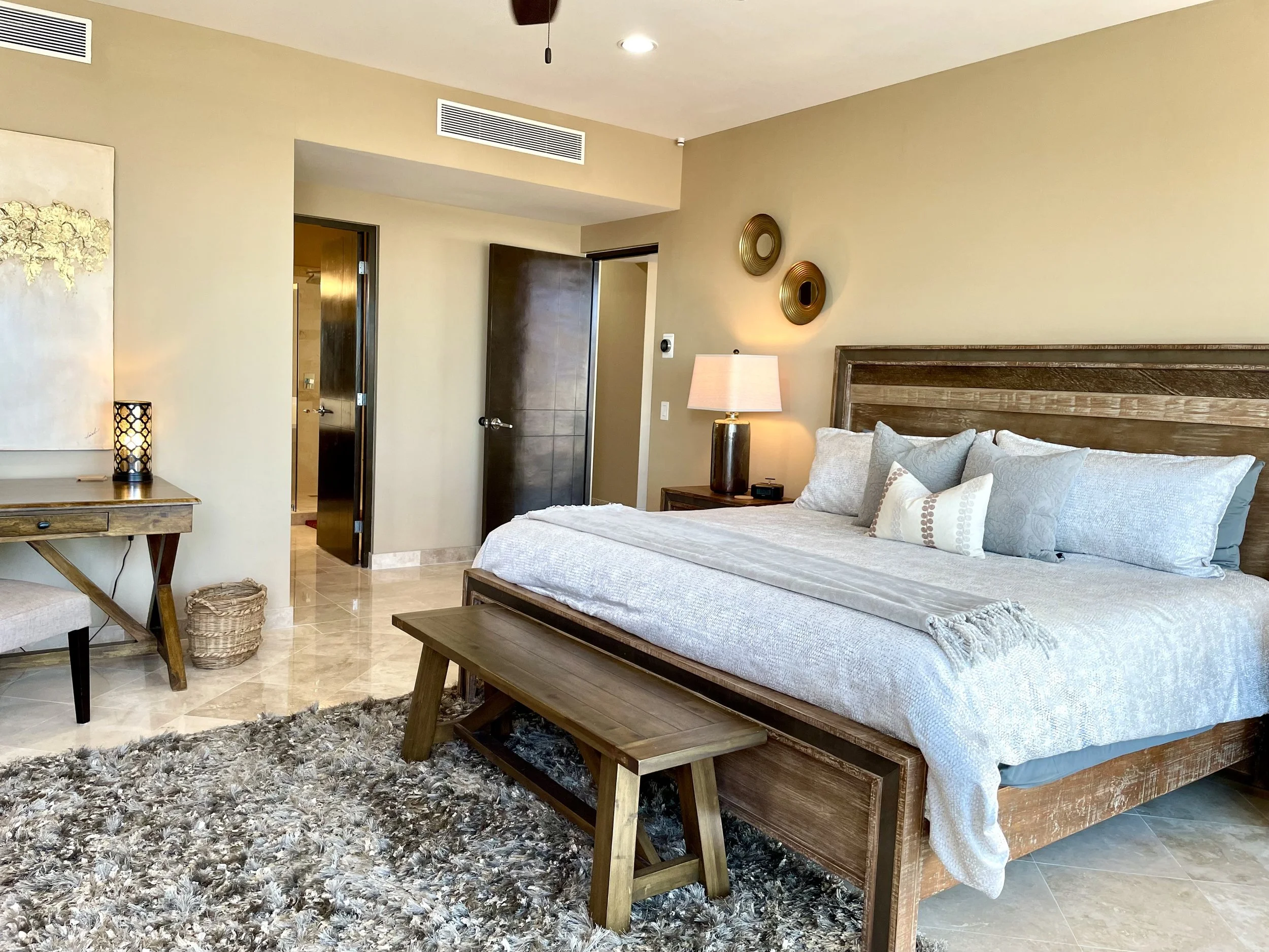 A bedroom with a wooden bed frame and white bedding, a nightstand with a lamp, decorative wall art, a shaggy area rug, and doors leading to other rooms.