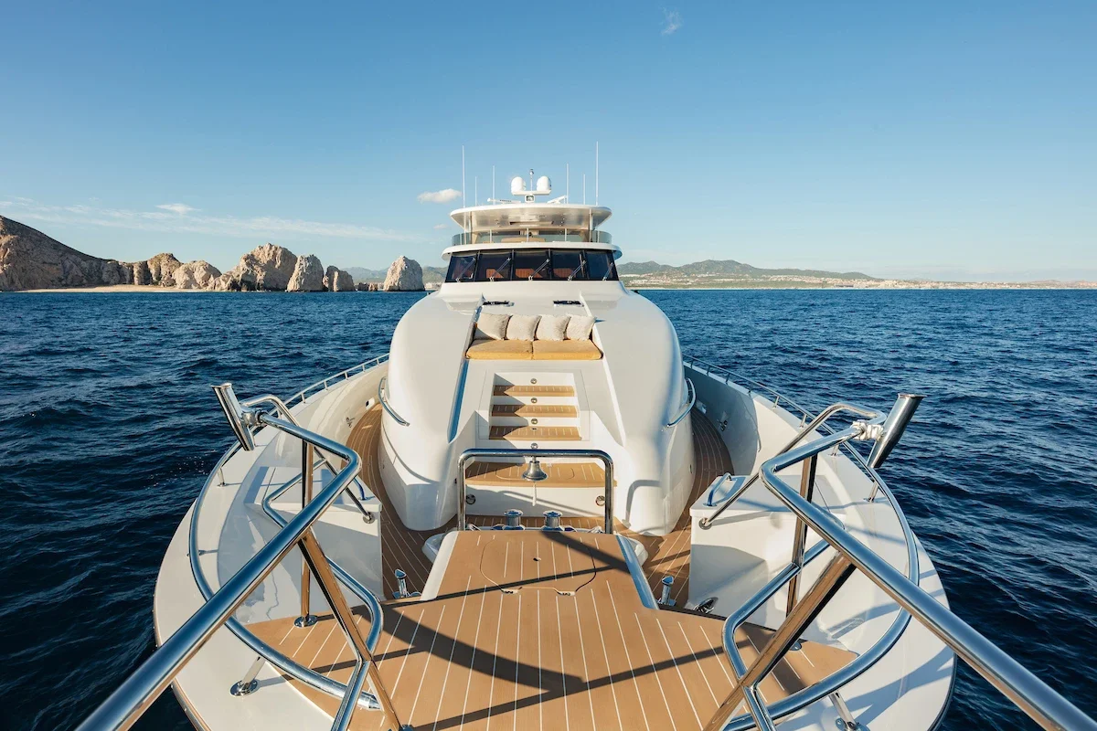 View of a luxury yacht on the ocean with rocky cliffs in the background, taken from the bow deck.