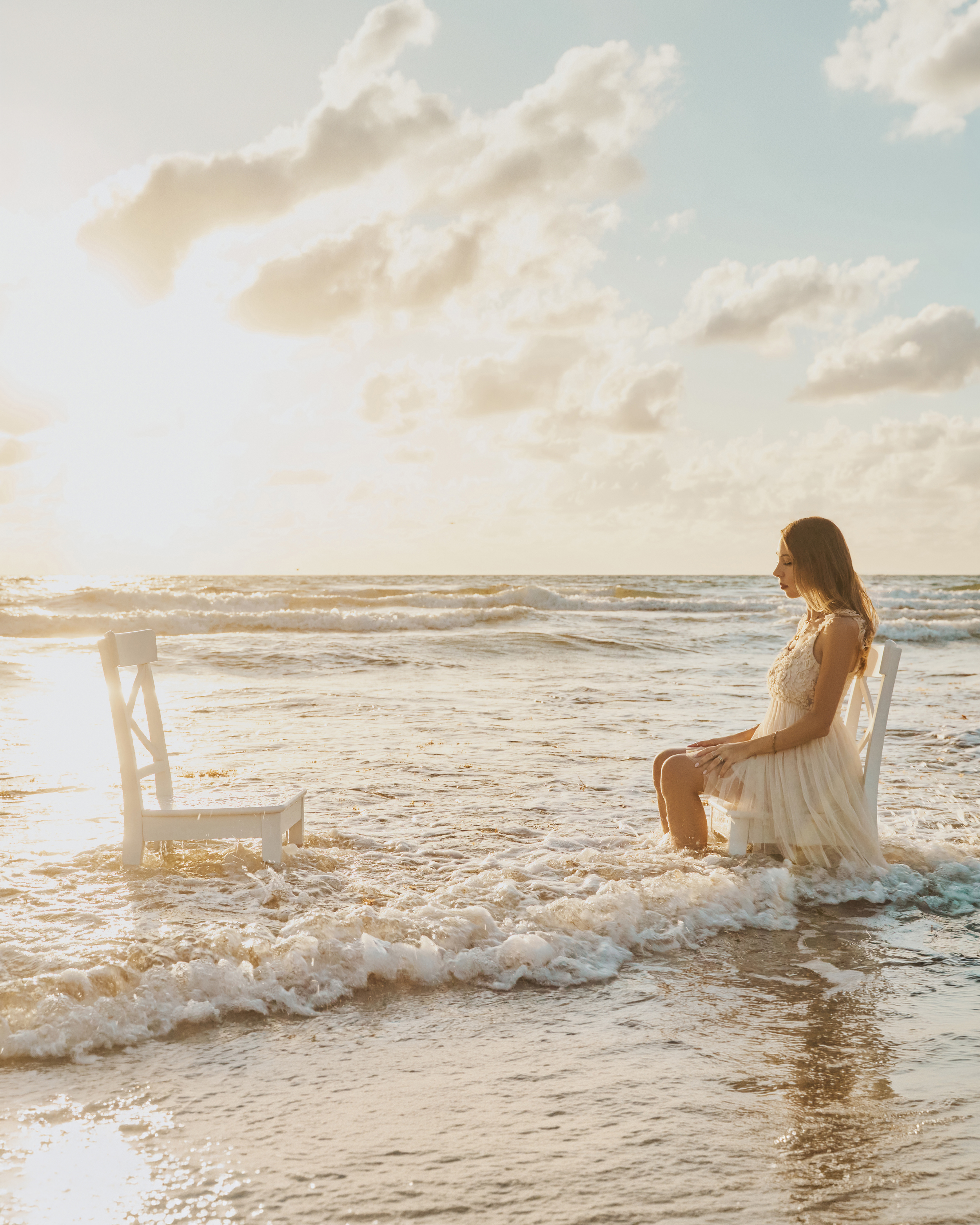 Alice sitting on a white chair in front of another white char in the ocean close to the shore.