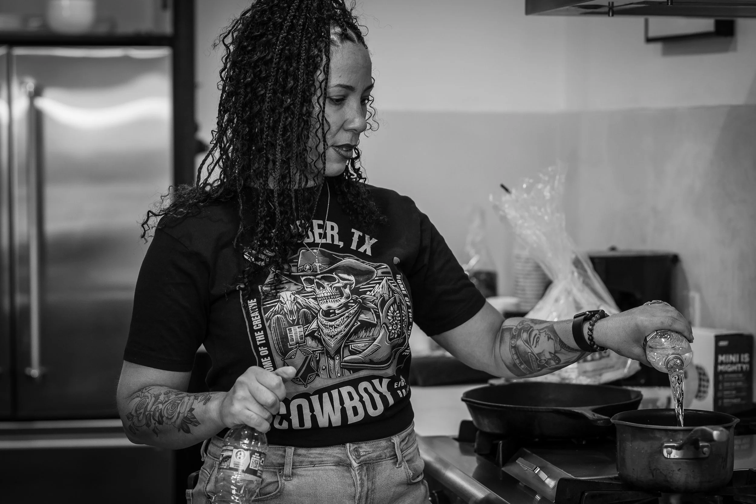 A woman with curly hair and tattoos on her arms is pouring syrup onto a plate.