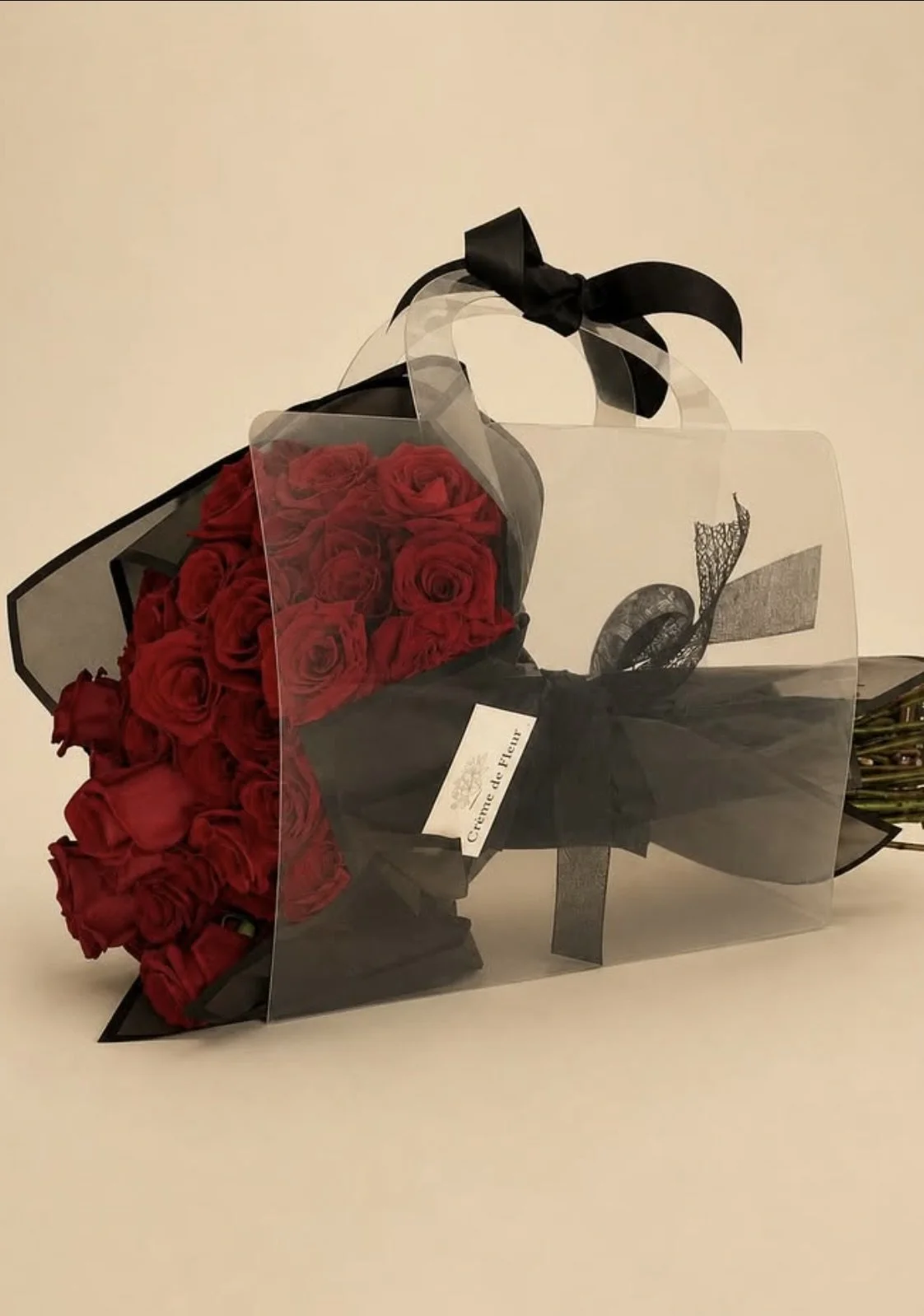 A bouquet of red roses wrapped in black and transparent paper with a black ribbon, sitting on a white surface.