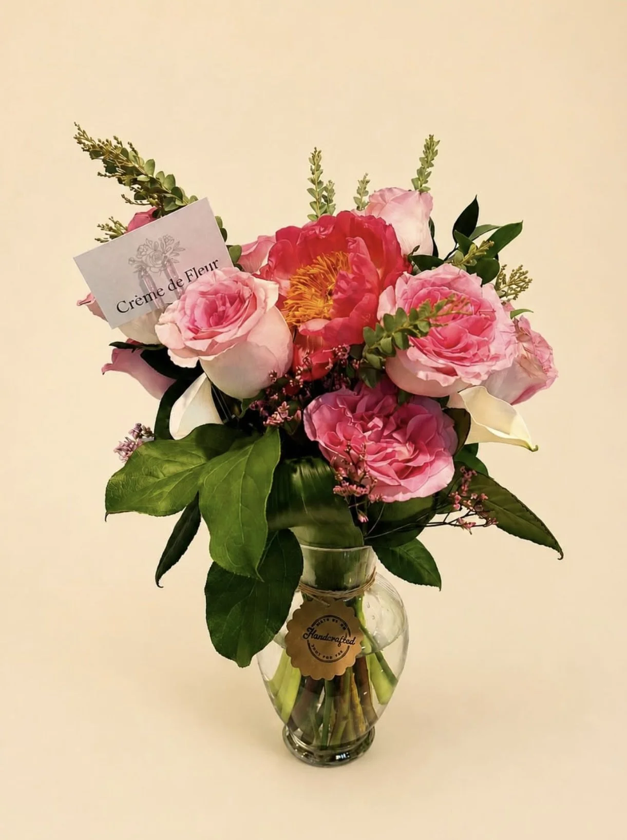 A bouquet of pink and red flowers with green foliage in a clear glass vase, with a white background.