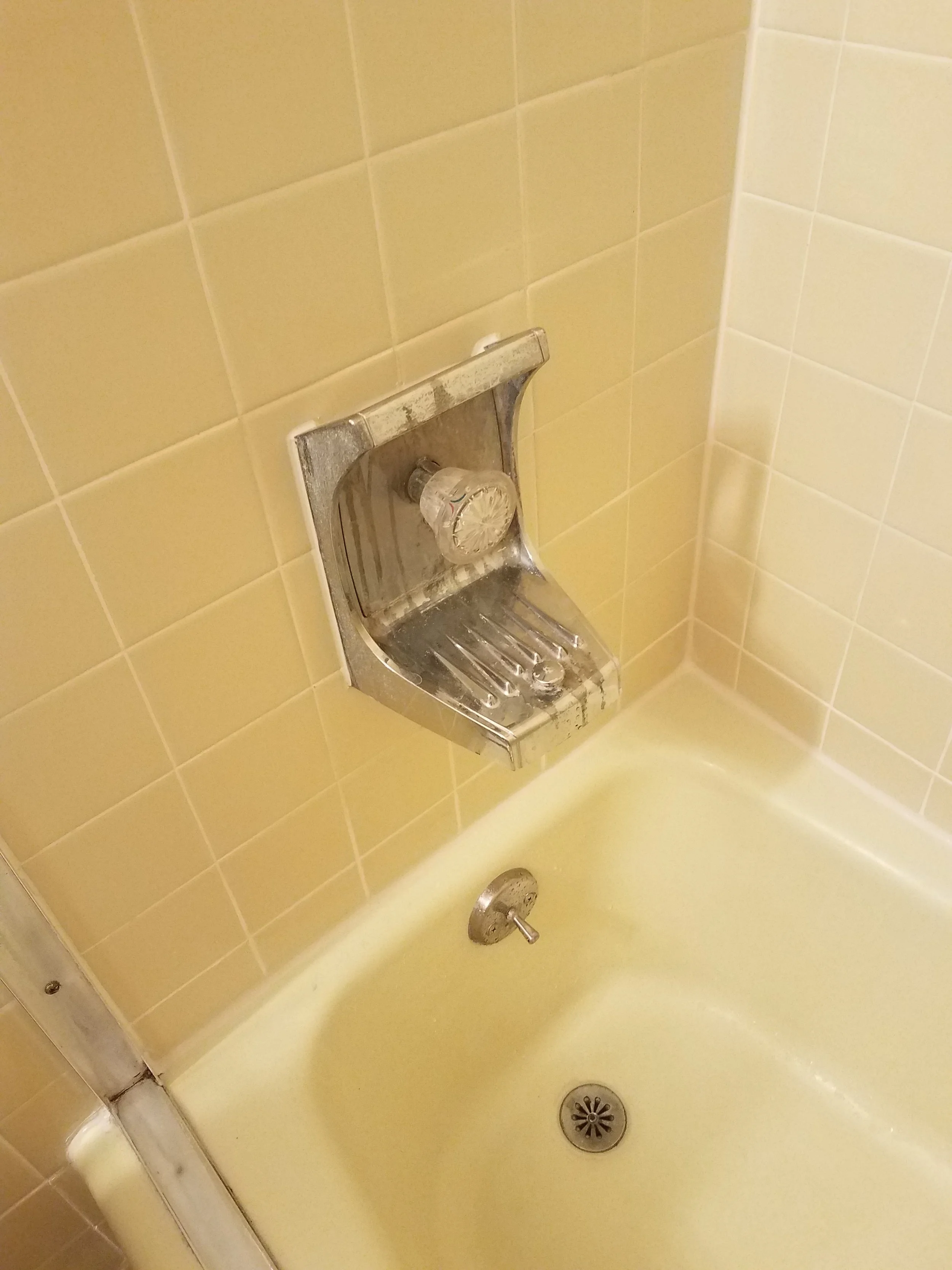 A yellow bathtub and shower area with beige tiled walls, a metal soap dish, and a silver shower drain on the floor.
