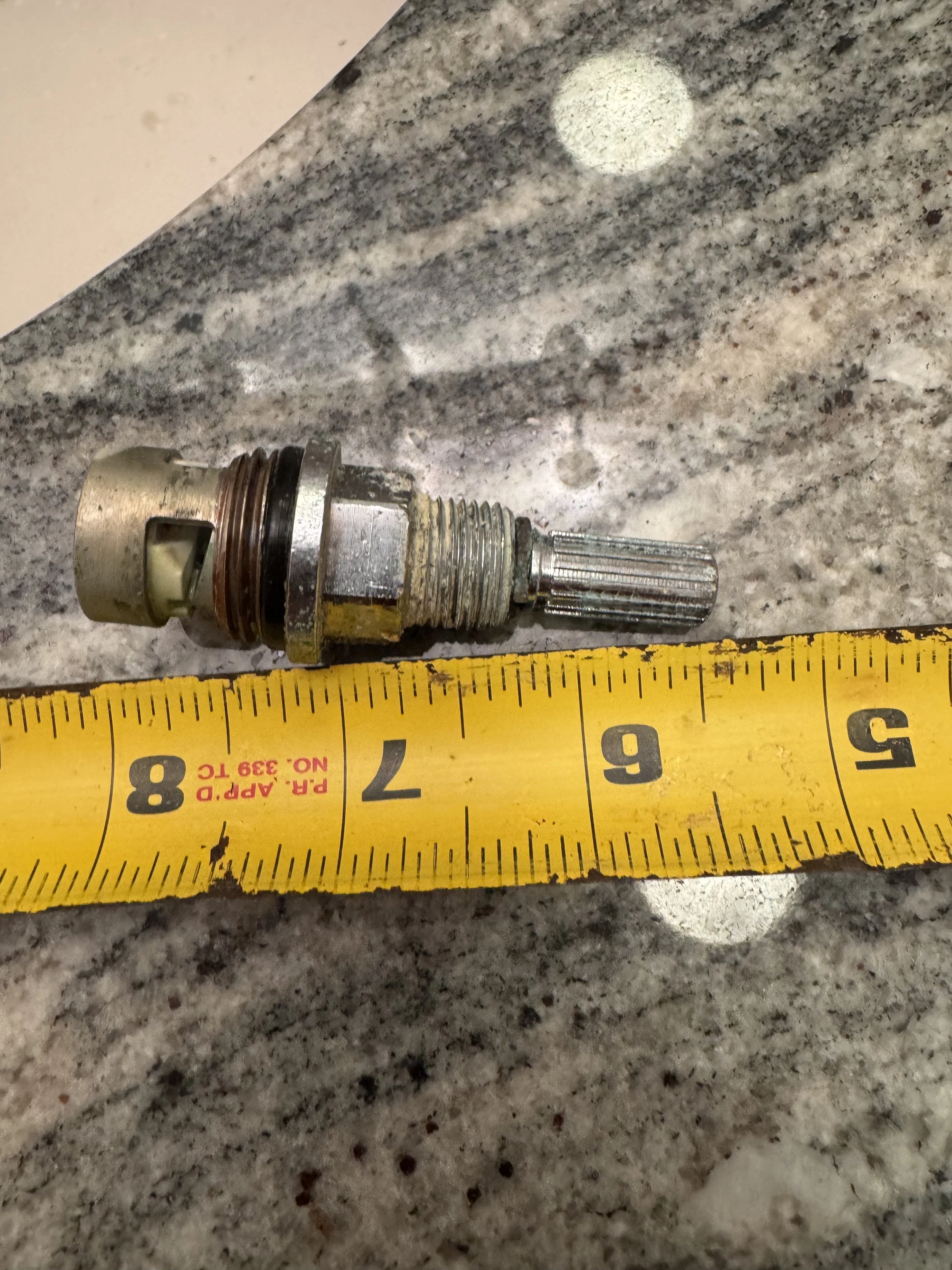 Close-up of a damaged spark plug on a granite countertop, with a yellow measuring tape beside it for scale.