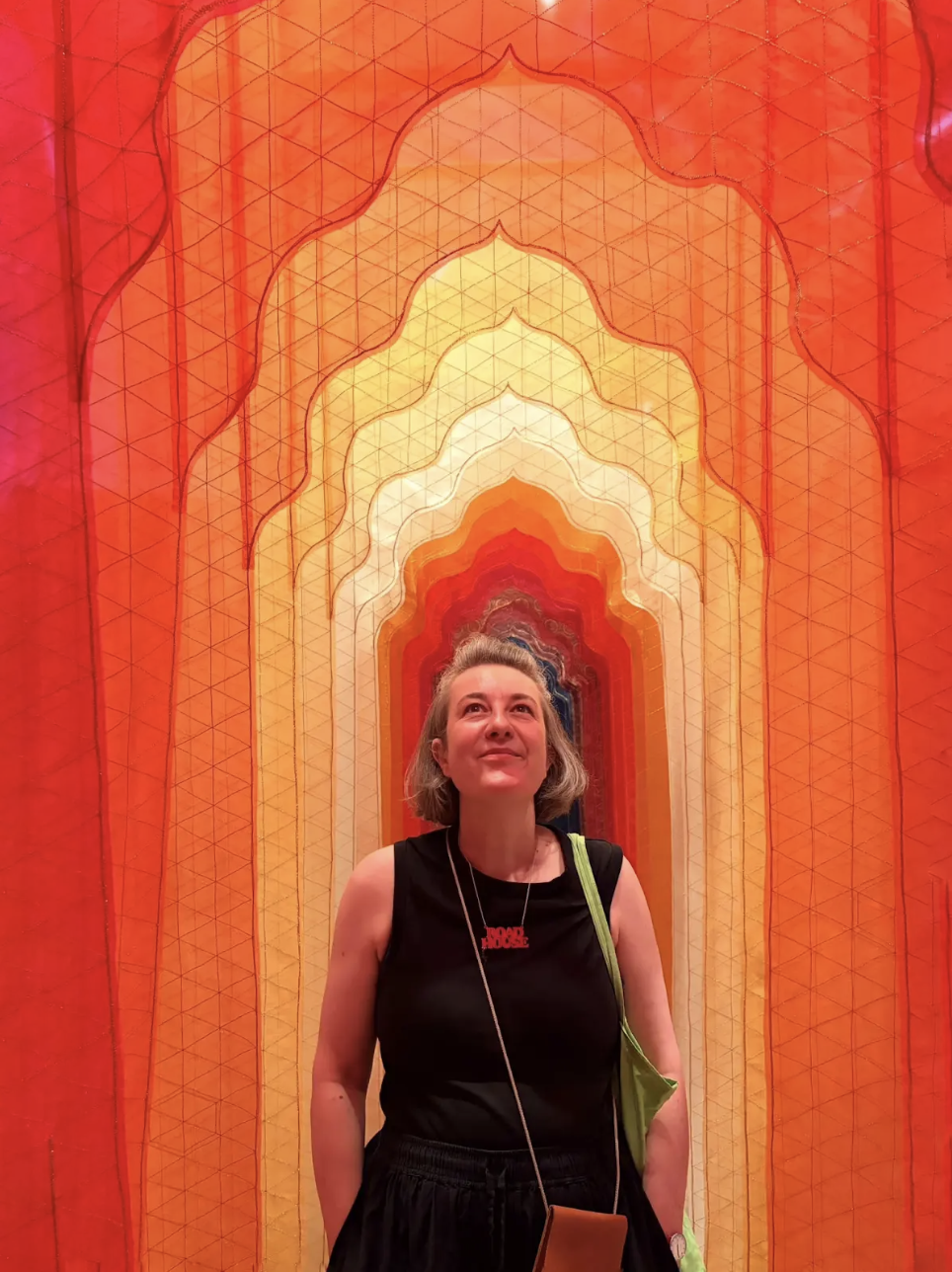 A woman standing in front of a colorful geometric tunnel installation with shades of orange, yellow, and white.