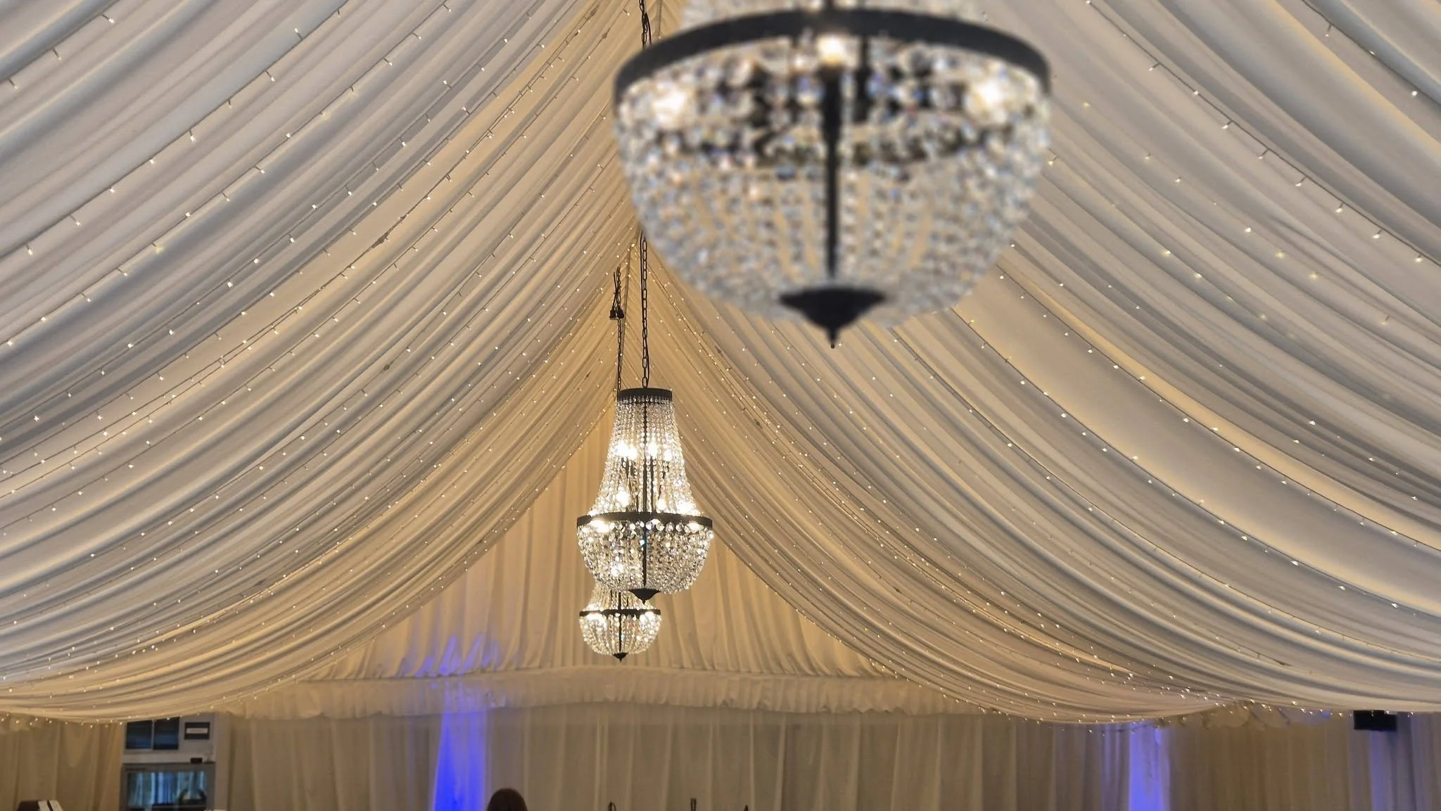 Elegant ceiling decorated with draped white fabric and adorned with multiple chandeliers.