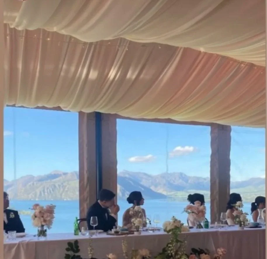 People sitting at a table during a wedding reception, with a scenic mountain and lake view in the background.