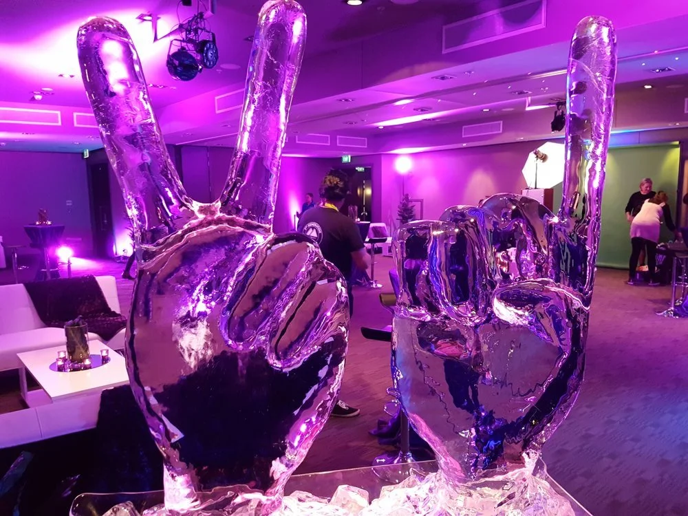 Ice sculptures of two hands making the peace sign, illuminated with purple lighting in a decorated event space.