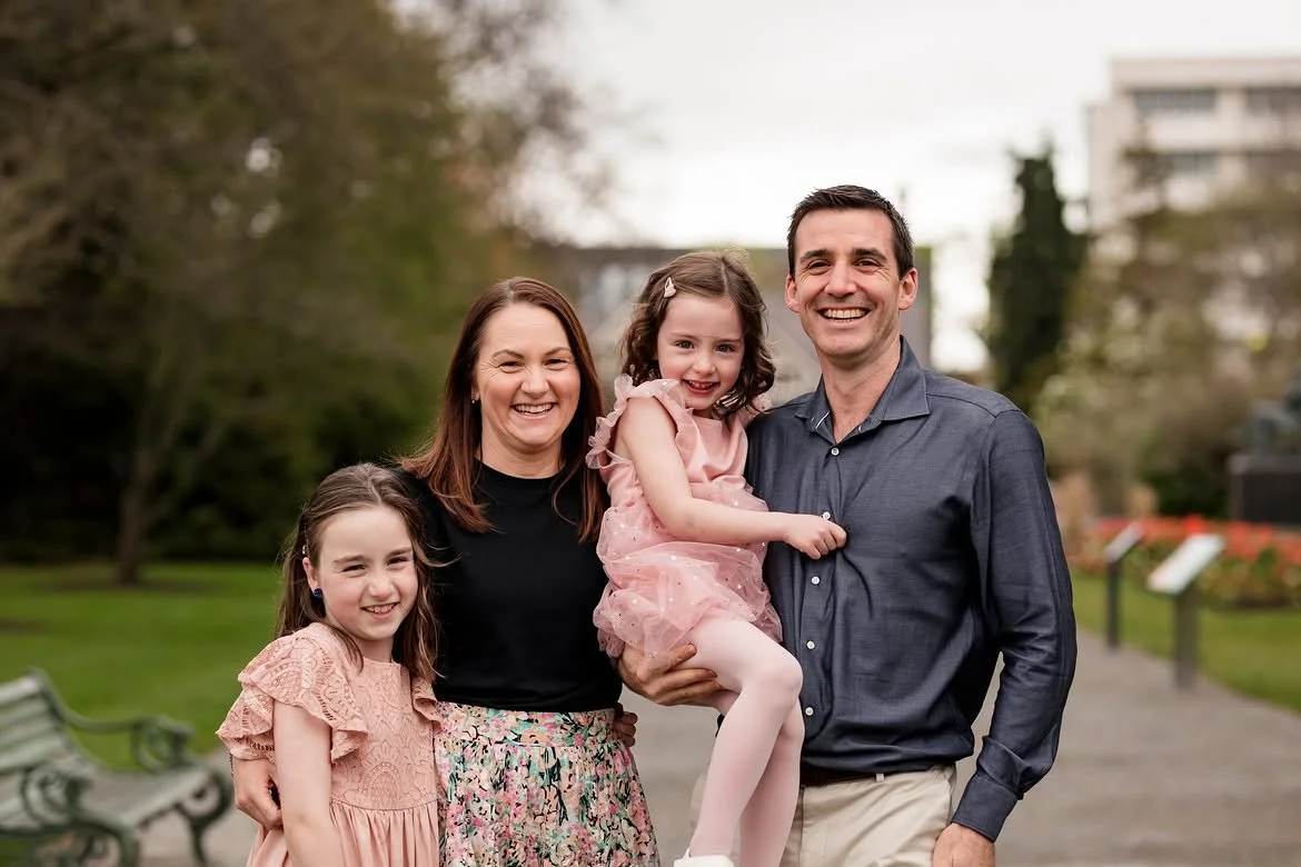 Happy family of four with two young girls and their parents outdoors in a park.