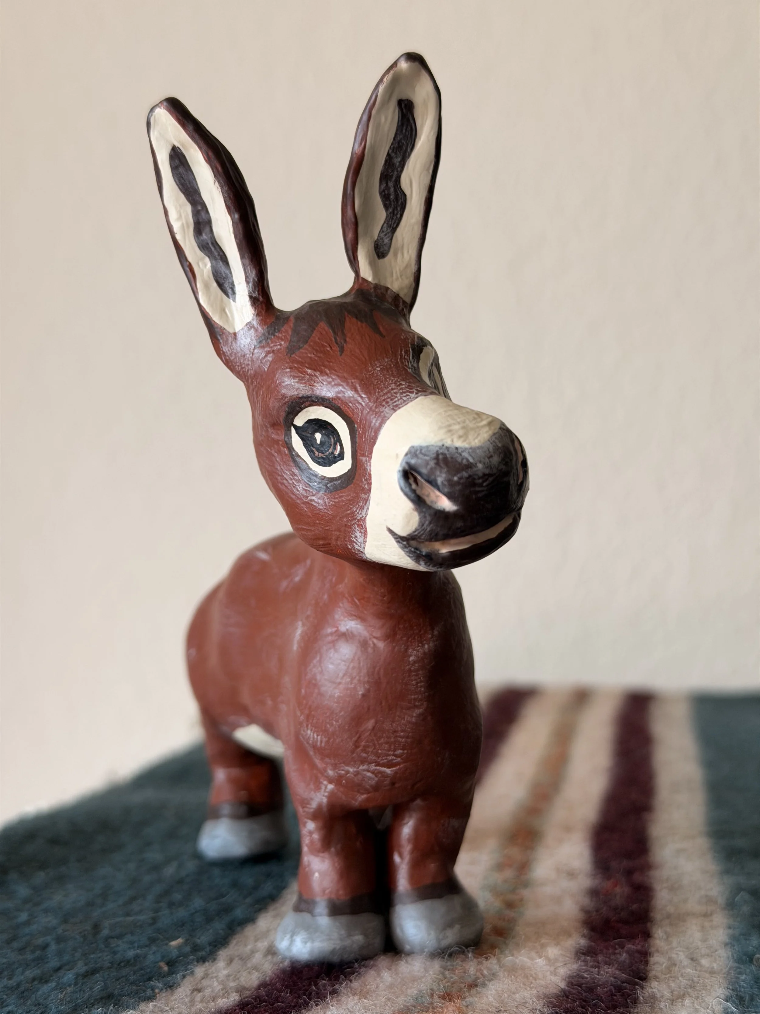 Painted wooden figurine of a deer with large ears, painted with black and white pattern on ears and face, standing on a multifaceted surface.