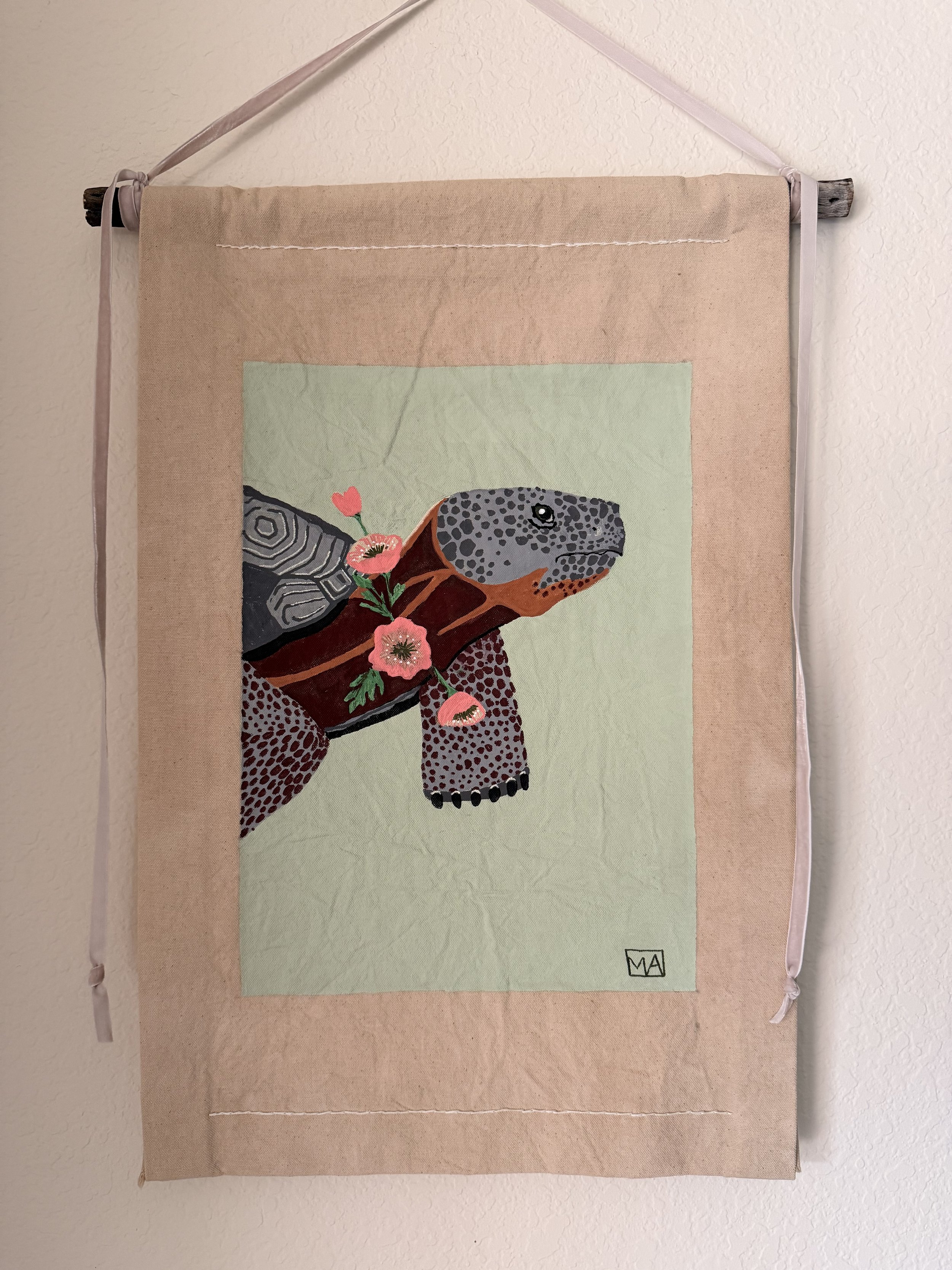 Wall hanging art depicting a stylized animal head, possibly a bear, with floral accents on a fabric background.