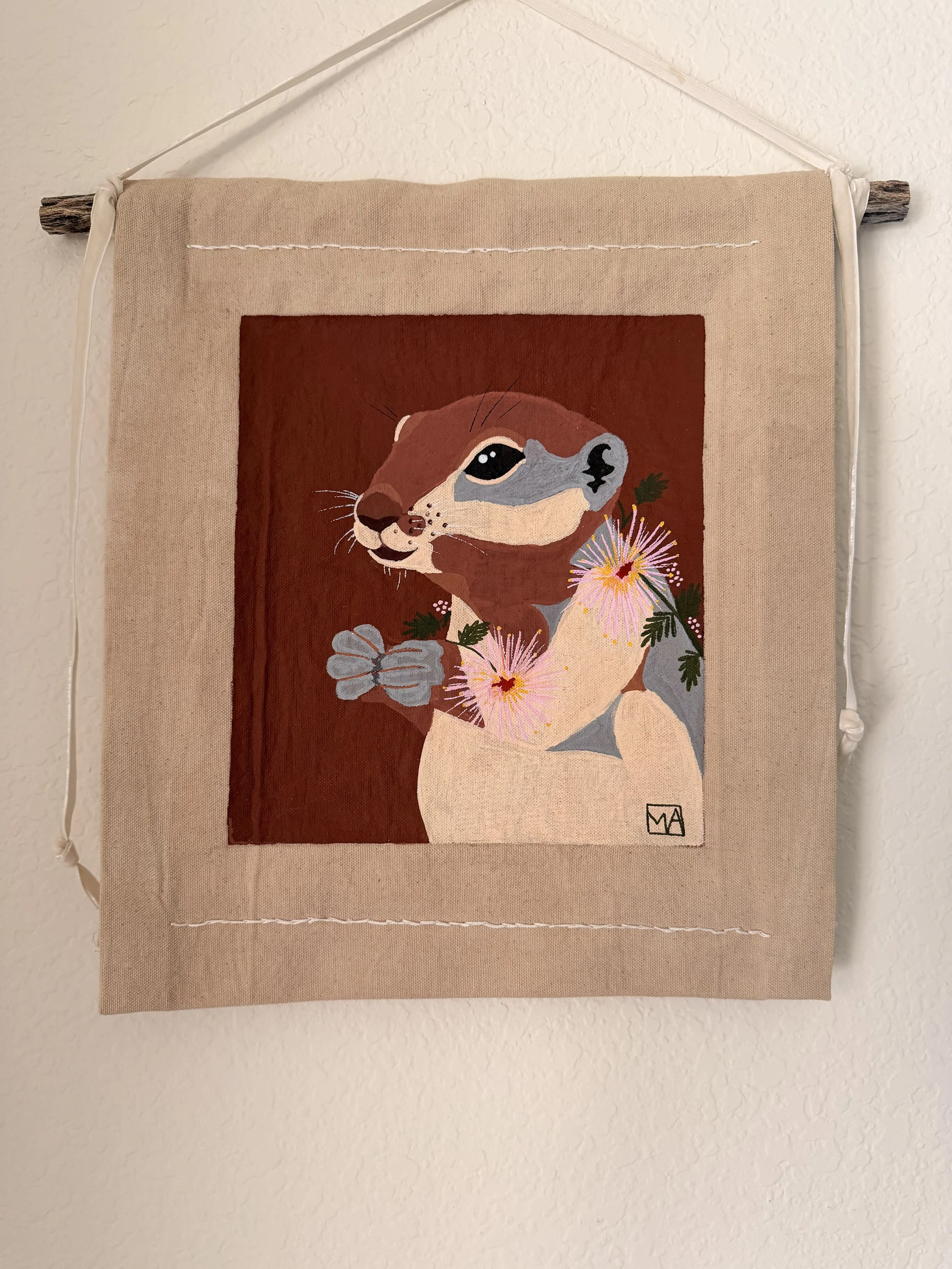 Art print of a dog with flowers, hanging on a wall with a wooden rod and string.