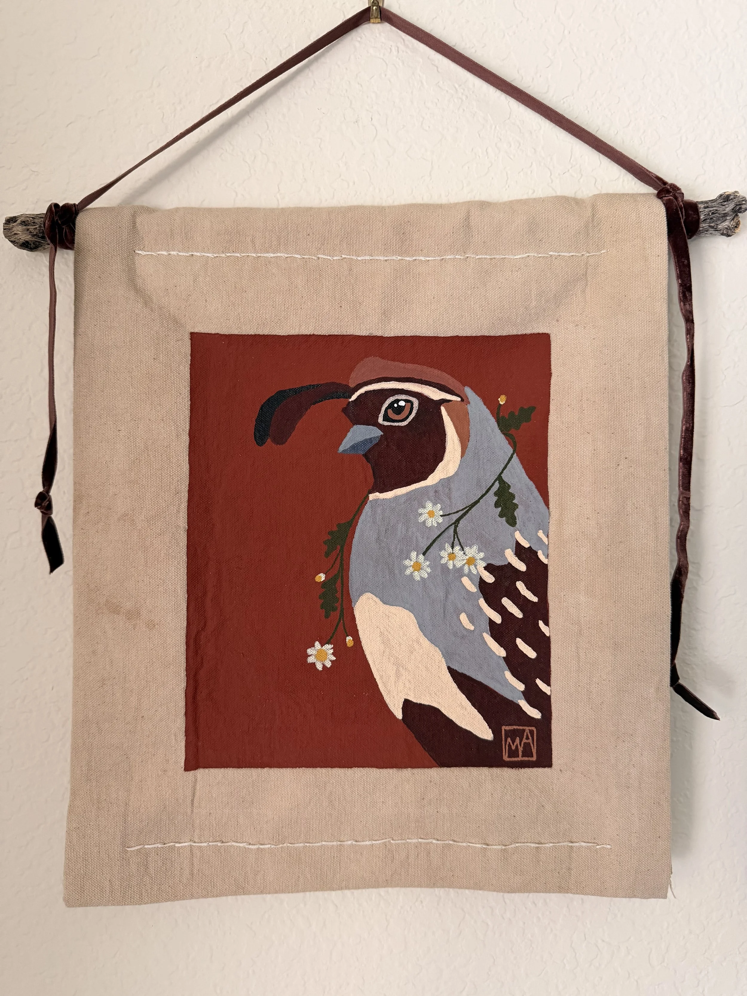 Wall hanging fabric art featuring a stylized bird with white, gray, black, and brown feathers, a blue beak, and a branch with white flowers and green leaves, on a red background.