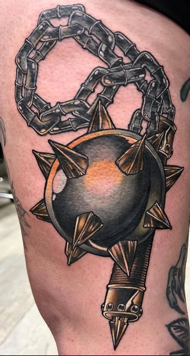 Tattoo of a large metal flail with spikes, attached to a chain, all in black and grey ink. Neo traditional tattoo.