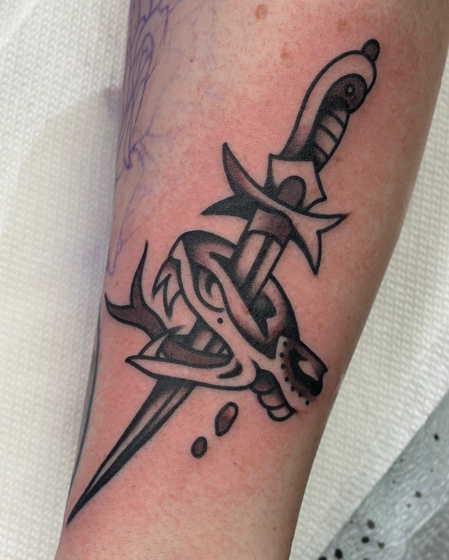 An American traditional black and grey tattoo of a stylized dagger through a snake head on someone's skin.