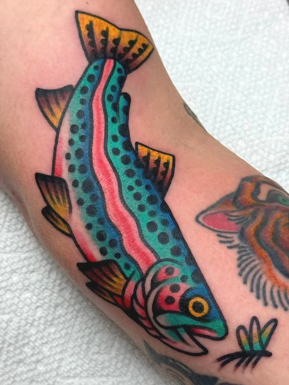 Colorful tattoo of a fish with blue, pink, yellow, and black details on a person's arm.