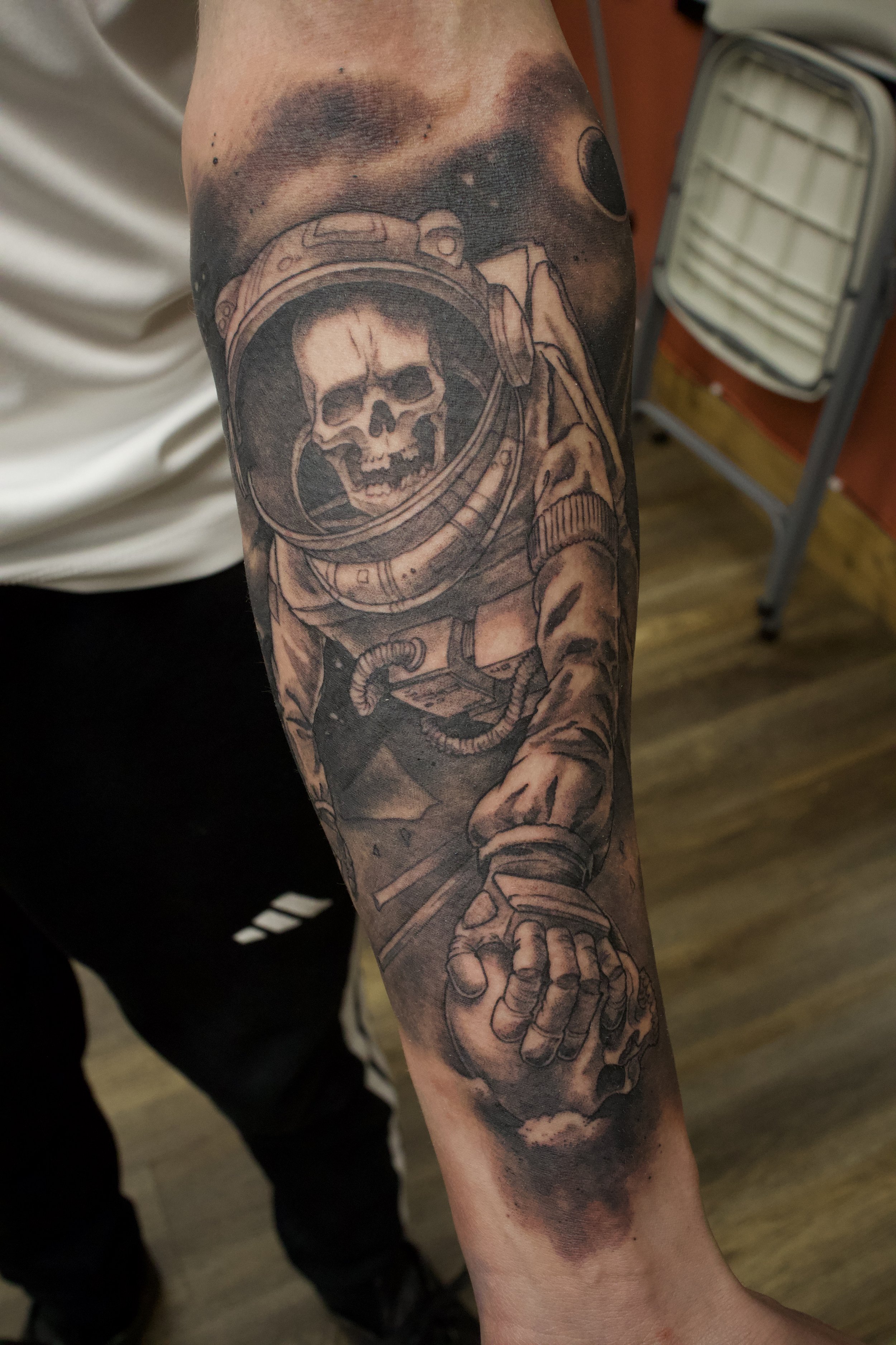 Tattoo of a skull wearing an astronaut helmet on the inner arm. Black and grey realism. 