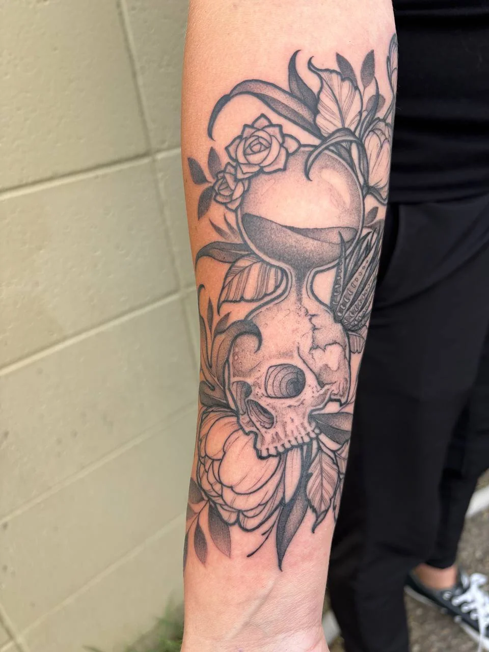 Tattoo of a skull with a rose, butterfly, and leaves on person's forearm.