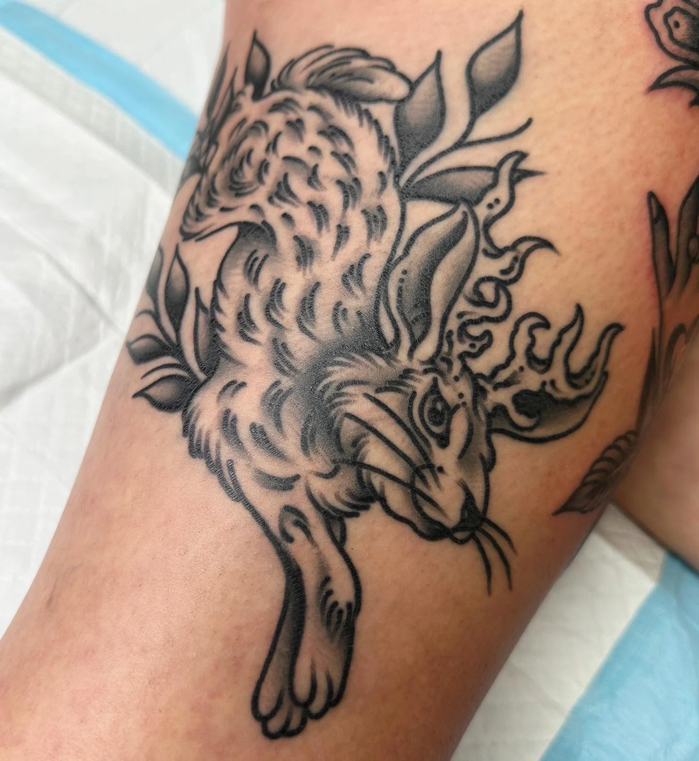 Black and gray tattoo of a jackalope surrounded by floral designs on a person's arm.