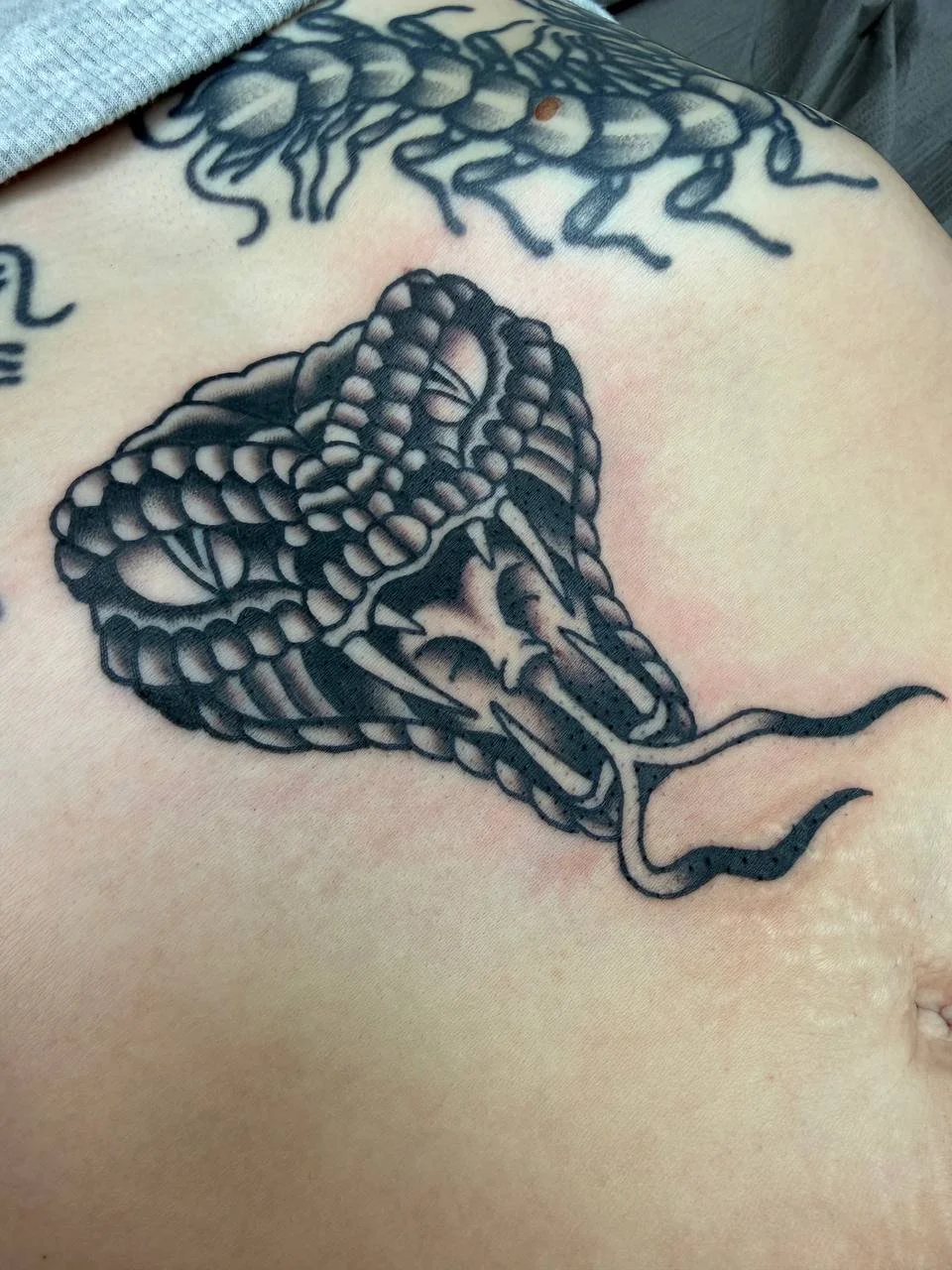 Black and gray tattoo of a cobra on a person's skin.