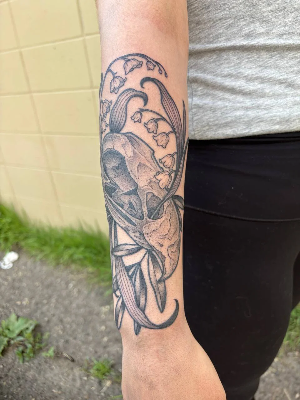 Tattoo of a human skull and flowers on person’s forearm, with detailed line work.