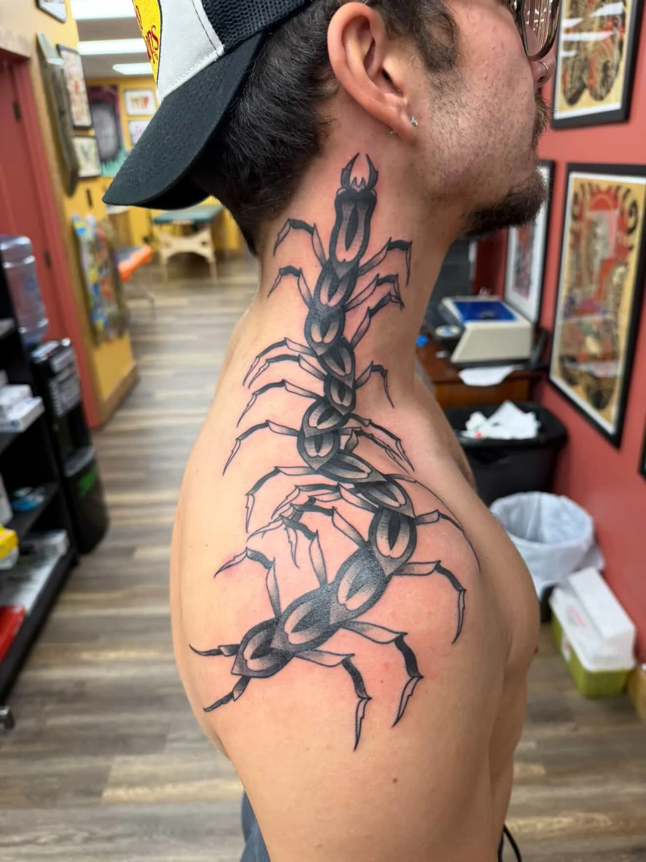 A man with a tattoo of a black centipede on his neck and shoulder in a tattoo shop. Black and grey custom blackwork tattoo.