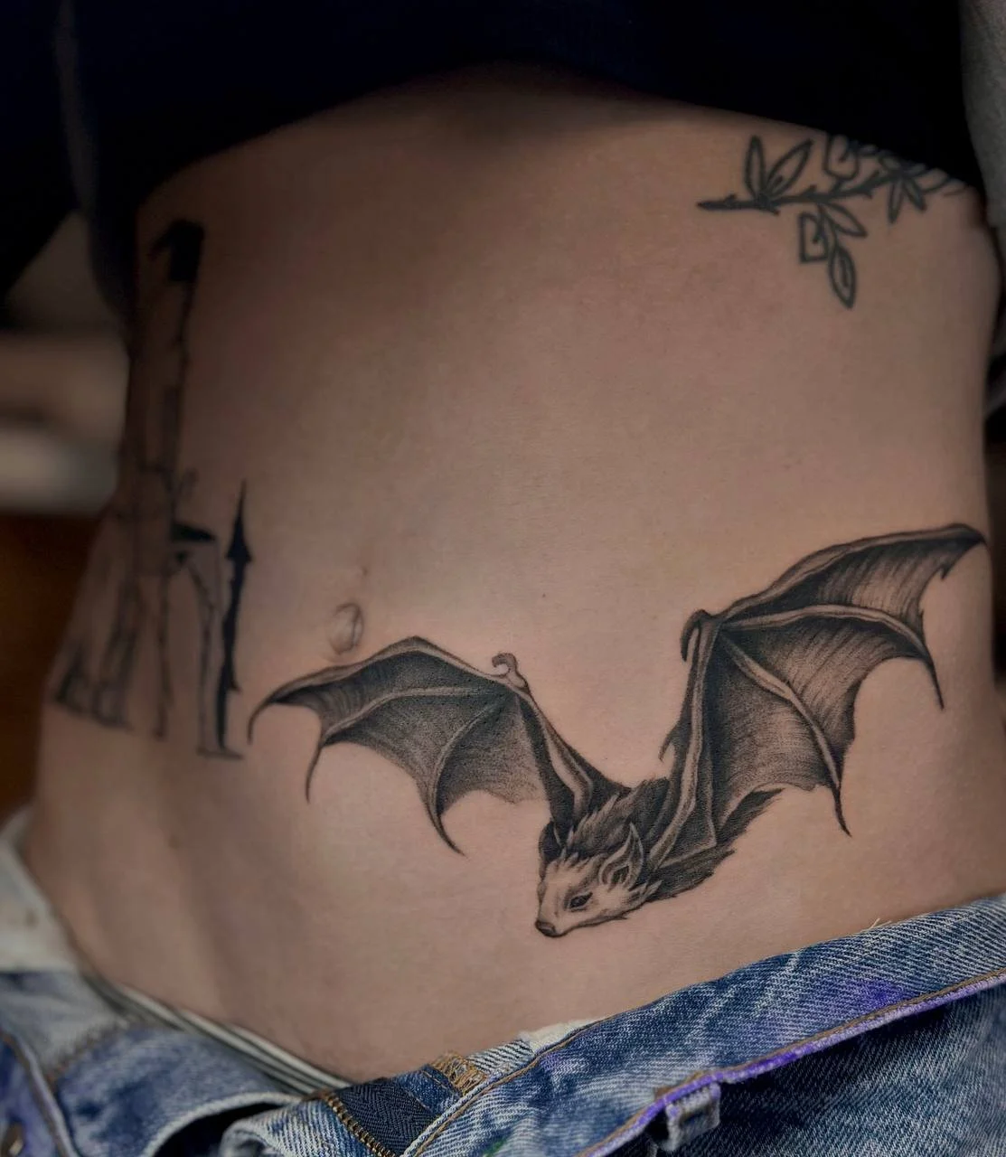 Tattoo of a bat with spread wings on a person's lower abdomen. Blackwork tattoo with stipple style shading.