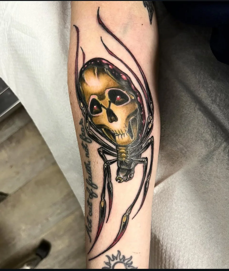 Tattoo of a spider with a skull face on its body. Colour neo traditional tattoo.