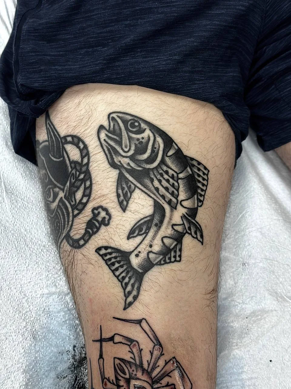 Tattoo of a stylized fish on a person's thigh. Black and Grey American traditional tattoo.