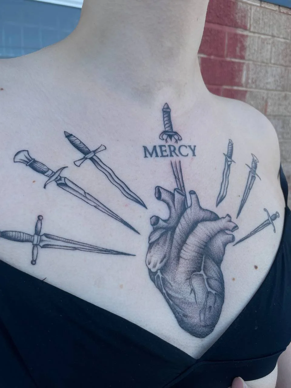 Tattoo of a human heart with nine swords piercing into it, and the word MERCY written above.