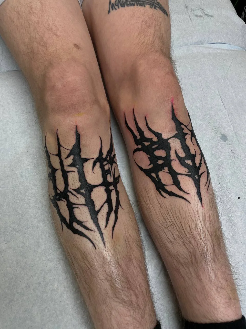 Tattooed legs with black tribal-style blackwork tattoos on the thighs.