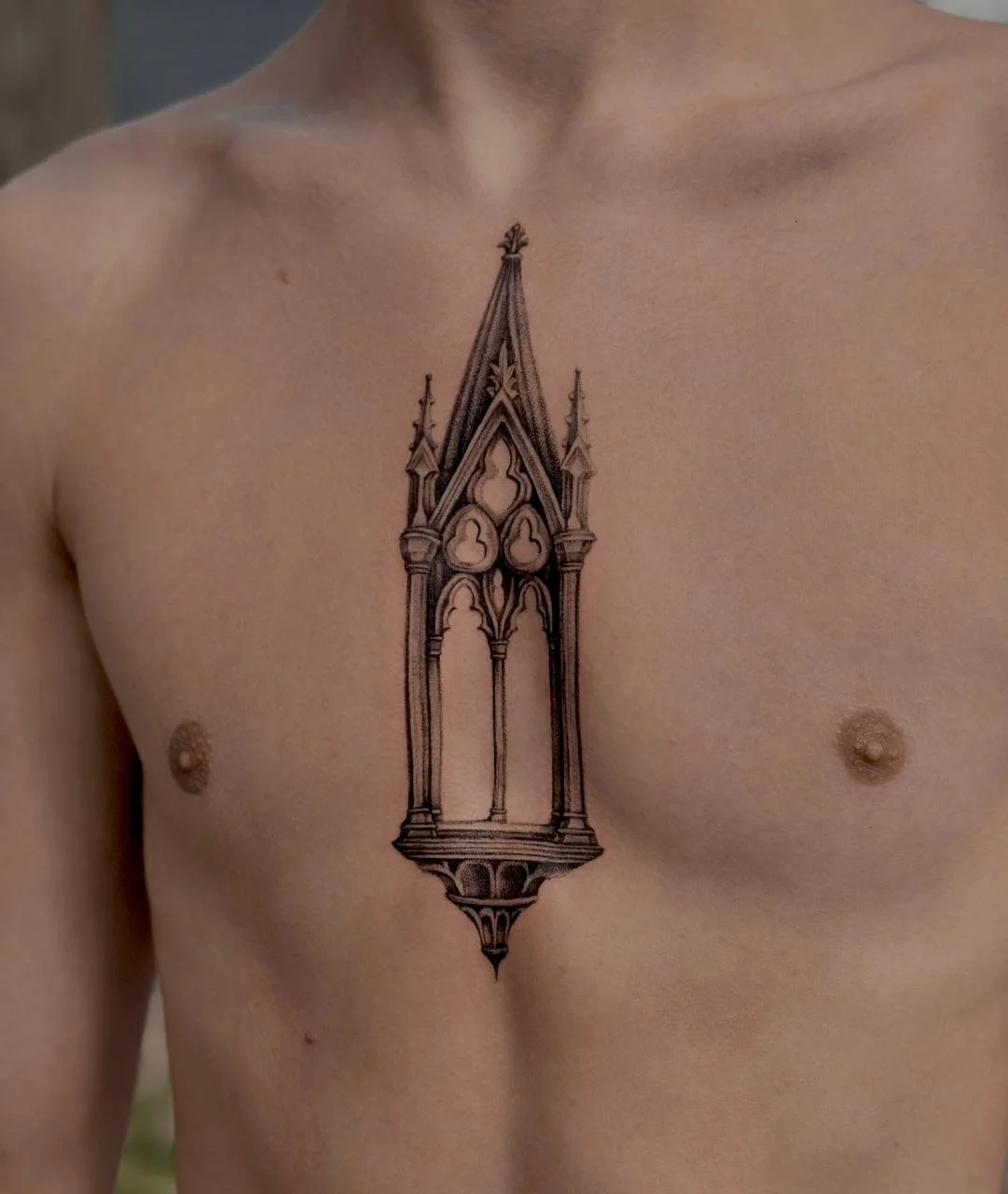 Tattoo of a Gothic-style architectural window on a person's chest. Stipple style shading blackwork tattoo.