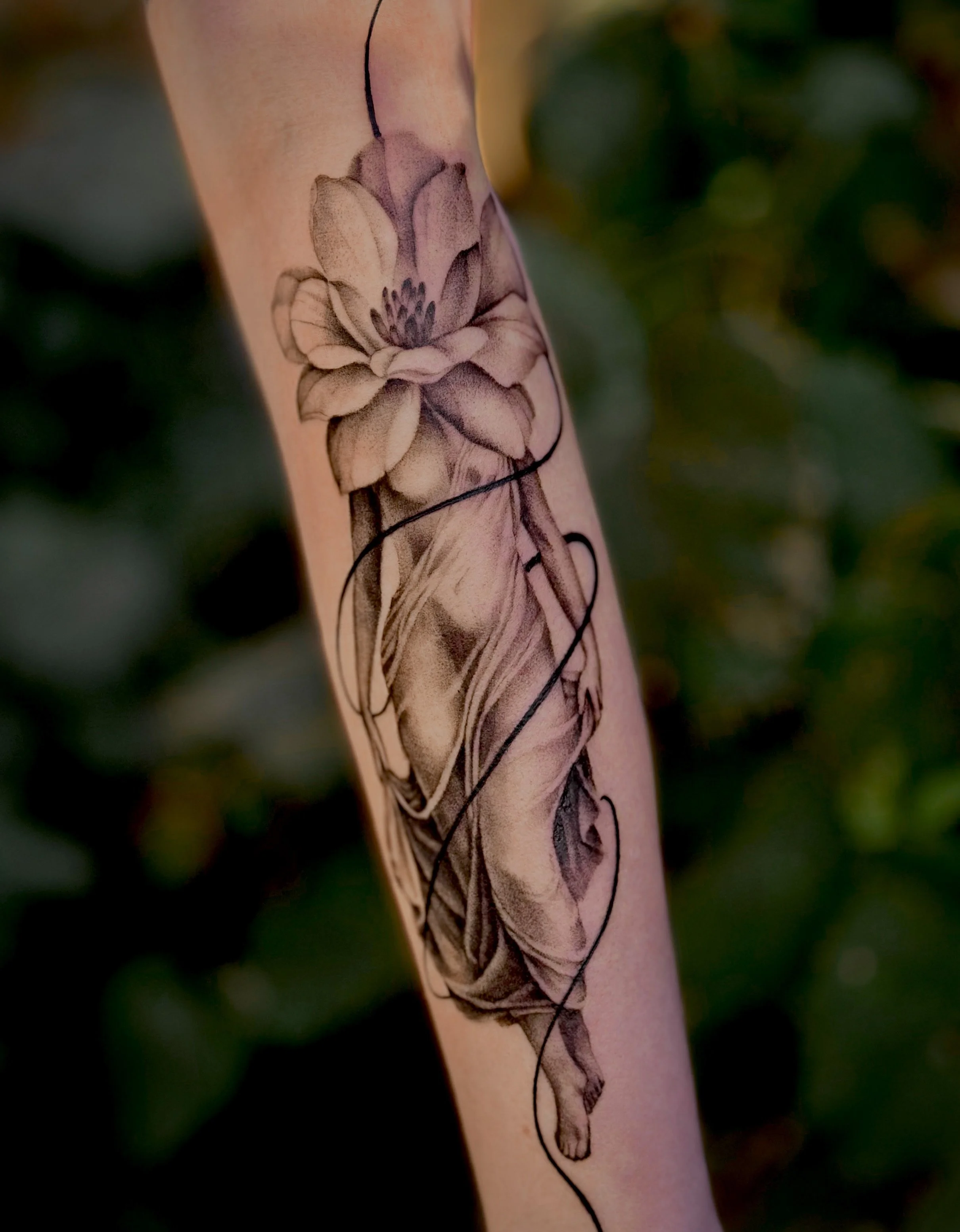 A tattoo of a detailed flower with petals and a stem on a person's arm. Stipple style blackwork tattoo.