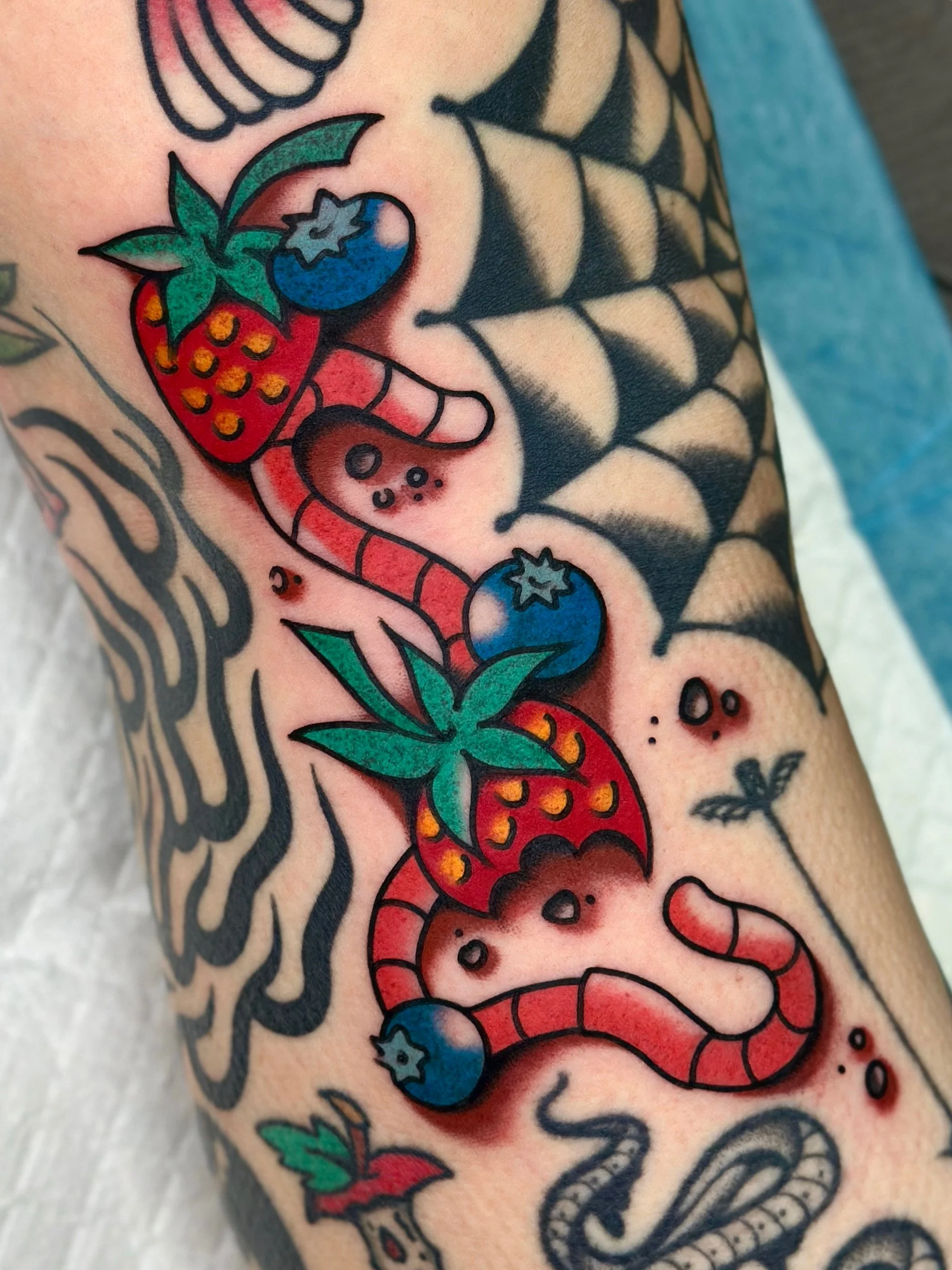 Colorful tattoo of strawberries, blueberries, and a worm on a person's arm.