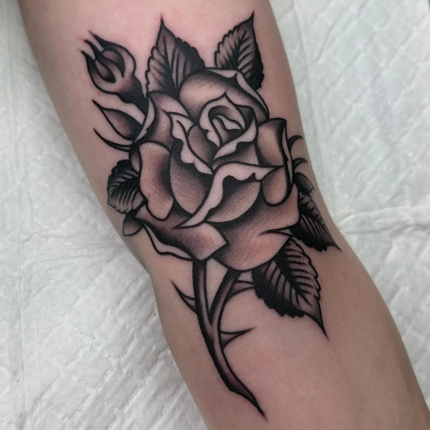 Black and gray tattoo of a rose with leaves on a person's arm.