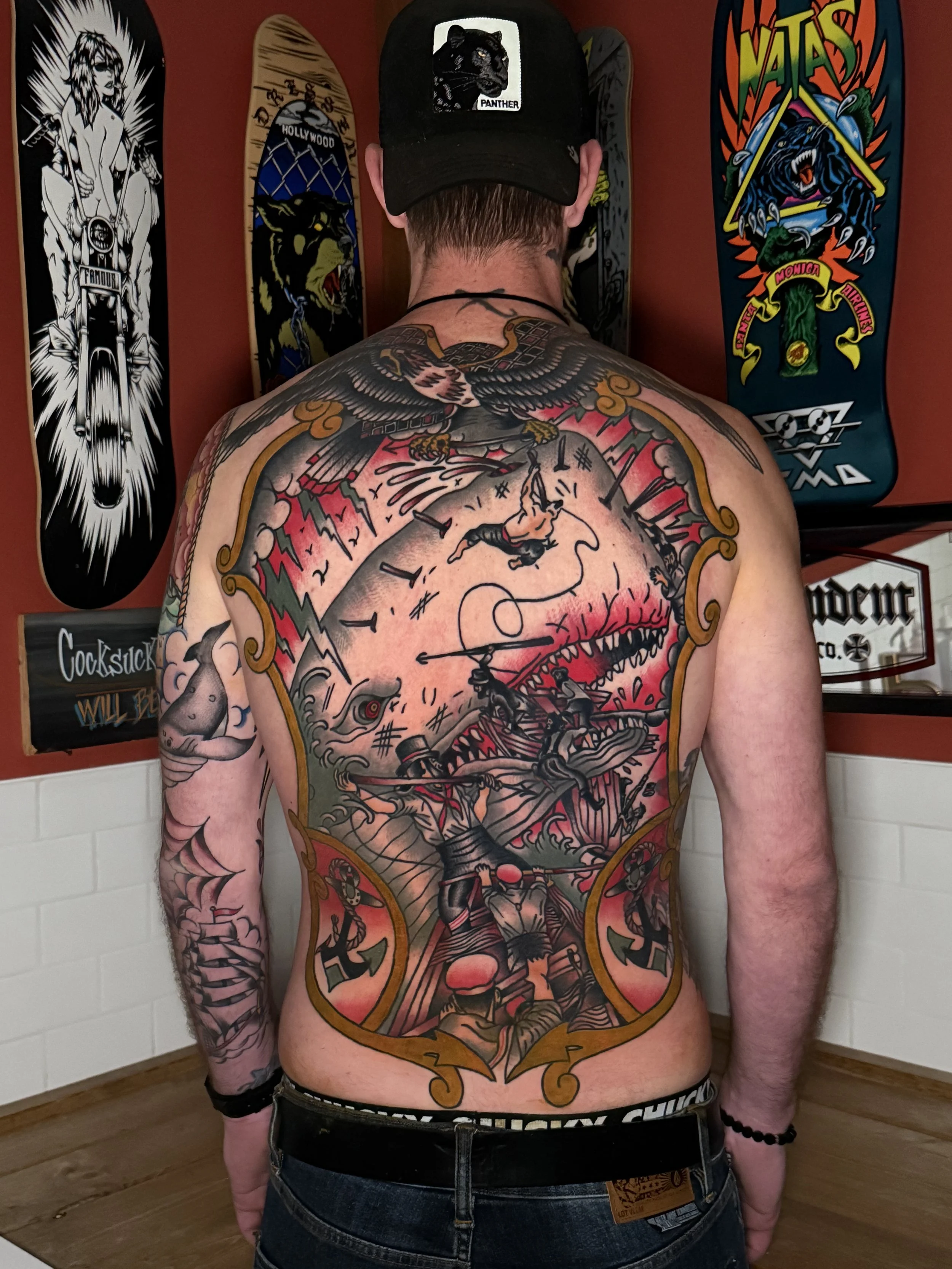 A person with extensive colorful tattoos on their back. Full colour American traditional tattoo back piece. Moby Dick vibes. A great battle of whaling. 