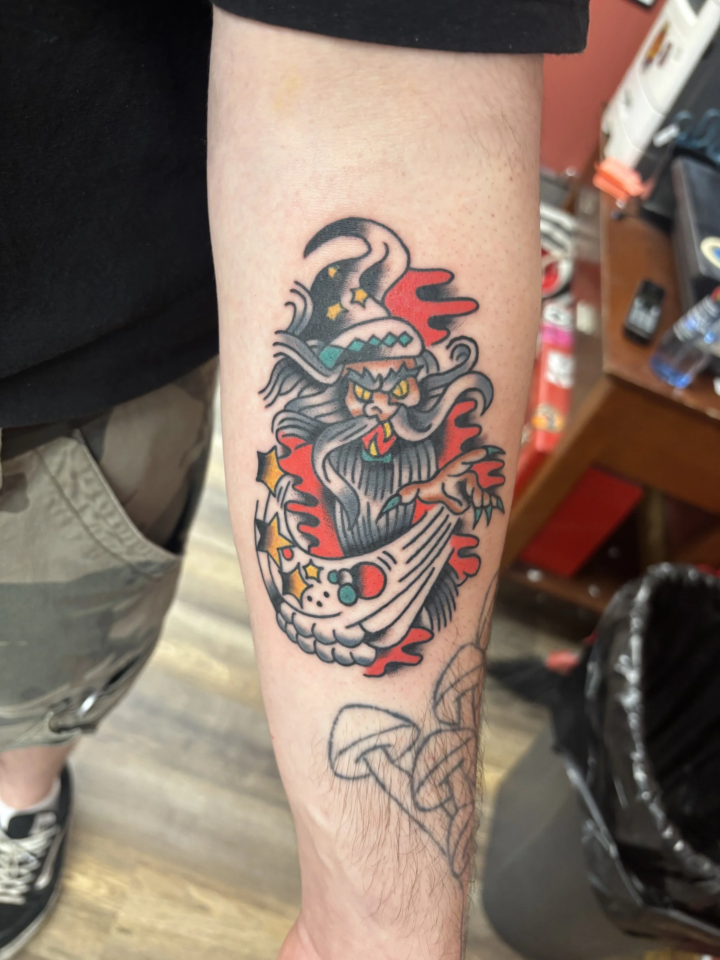 Tattoo of a fierce wizard with black, red, and teal colours on a person's forearm. Bold and full colour traditional tattoo.
