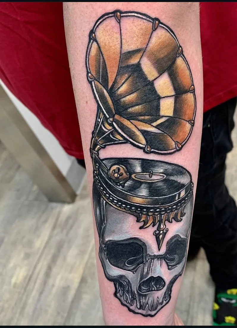 Tattoo of a vintage gramophone with a horn above a human skull. Full colour neo traditional tattoo.