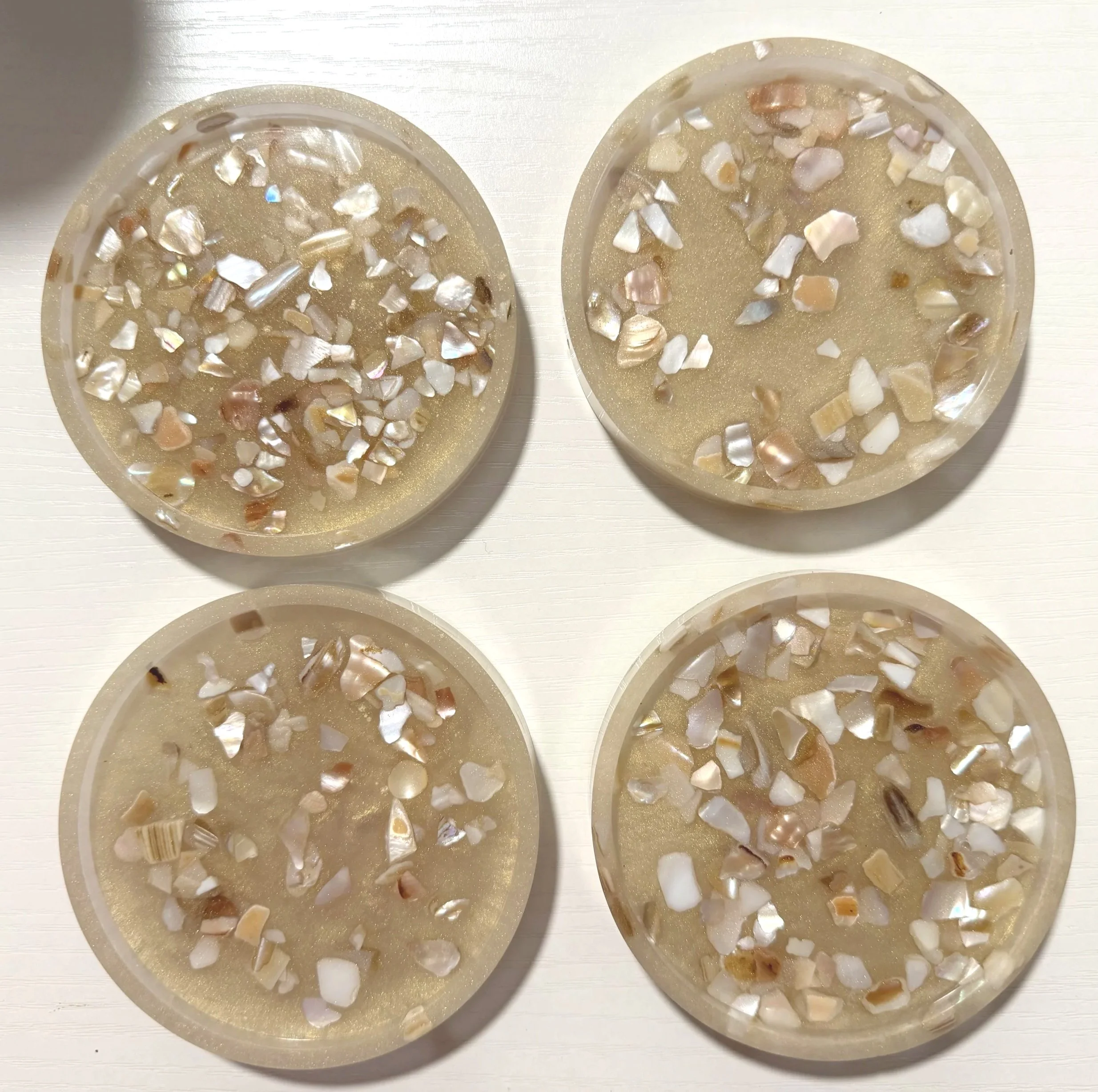 Close-up of two circular resin jewelry pieces embedded with small iridescent shell fragments, placed on a white surface.